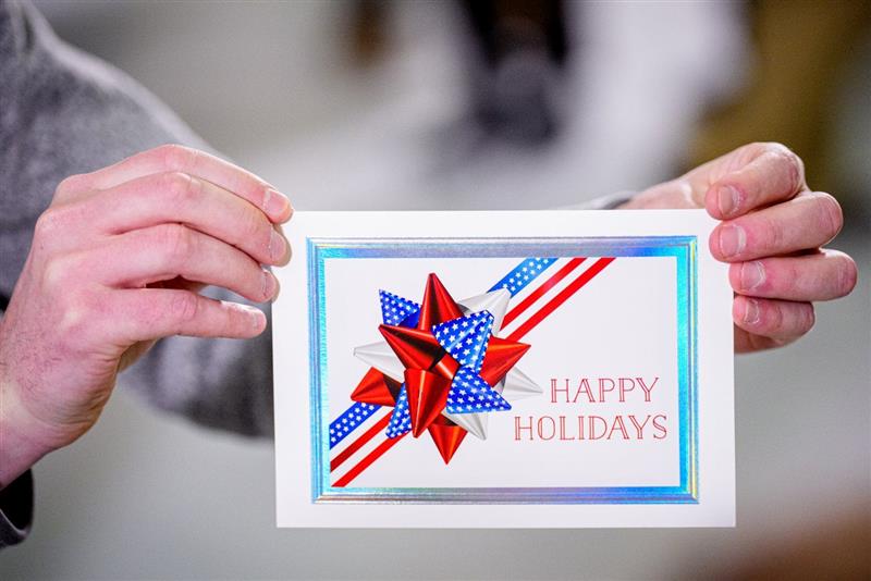 Hands holding a Gallery Collection patriotic holiday greeting card featuring a red, white, and blue star design and the message ‘Happy Holidays.